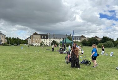 People enjoy Sports Fun Day on a grassy field with bikes and games near large buildings.